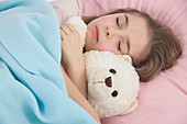 Girl asleep in bed holding teddy bear