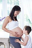 Pregnant woman with son kissing tummy