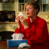 Rhinitis: woman sneezes into a tissue