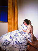Fearful woman clutching a duvet in a corner