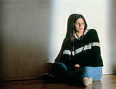 Depressed teenage girl sits on the floor indoors