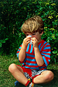 Young boy with hay fever (rhinitis) blows his nose