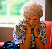 Loneliness: elderly woman clasping face in hands