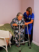 District nurse helps old woman use walking frame