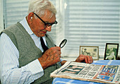 Elderly man uses a magnifying glass to read paper