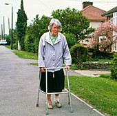 Old woman walks along street using walking frame
