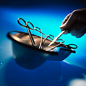 Hand places scalpel with forceps in a metal bowl