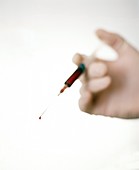 Gloved hand holds syringe filled with blood sample
