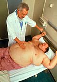 Hospital doctor examines obese man lying on a bed