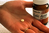 Pill of folic acid on woman's hand next to bottle