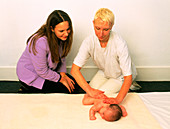 Therapist massaging back of baby watched by mother
