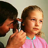 Doctor examines ear of young girl using otoscope
