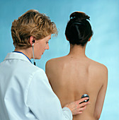 Female GP using stethoscope on young woman's back