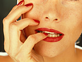 Woman's mouth biting her nail-varnished nails