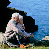 Elderly couple sit at the top of a rocky coast