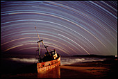 Star trails over rusted boat wreck