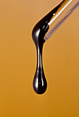 Drop of crude oil falling from glass tube