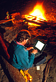 Man using a laptop computer by a campfire