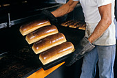 Baker removing bread from an oven