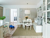 weiße Wohnküche im Landhausstil mit gemütlicher Sitzbank, Vitrinenschrank und Fliesenboden