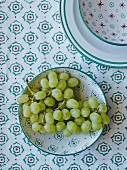 Weintrauben in Schale mit grün-rotem Muster auf gleich gemusterter Tischdecke