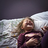 Lachendes kleines Mädchen in Schlanfanzug liegt auf Bett