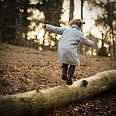 A little girl in a grey coat balancing on a log in the forest