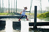 A little girl jumping across a body of water from wooden poles onto a jetty