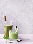Two green smoothies garnished with olives and cucumber sticks
