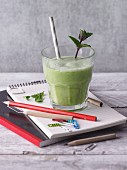 A green smoothie with a sprig of mint on school utensils