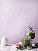 Two green smoothies garnished with figs and leaves
