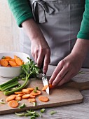 A woman chopping carrots and celery on a chopping board