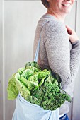 A woman carrying a shopping bag full of green vegetables