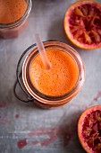 Blood orange smoothie in a glass jar with a straw