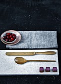 Chocolates and cutlery on marble board and small bowl of cranberries on cloth