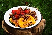 Grilled vegetables on a plate on a tree stump in grass
