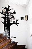 Rustic wooden staircase and black family tree painted on white wall and decorated with family photos