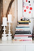 Lit candles in two white candlesticks and stacked books on sideboard