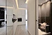 Open-plan hall area in designer apartment with white, fitted kitchen counter, sliding door and view into bathroom