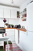 Corner of white kitchen with wooden worksurface, bracket shelves and wall cabinets