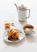 Croissants, Aprikosenkonfitüre im Glas, Kaffeetasse und Kaffeekanne