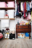 Clothing hung in open-fronted wardrobe above retro cabinet next to storage bins above stacked shoes