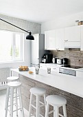 Kitchen counter with white worksurface and white bar stools against rustic wooden cladding