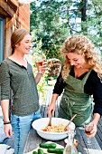 Cheerful young women with pasta salad and wine in garden