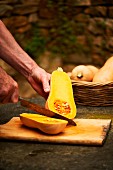 A man halving a butternut squash on a wooden chopping board