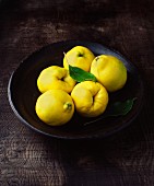 Five quinces with leaves in wooden bowl