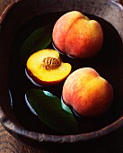 Whole and halved peaches with leaves in vintage wooden bowl of water
