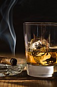 A smoking cigar next to a glass of whiskey