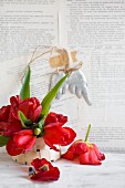 Red tulips in chip-wood basket against wall papered with book pages