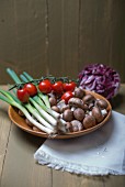 Champignons, Kirschtomaten und Frühlingszwiebeln in Holzschale auf Holzuntergrund